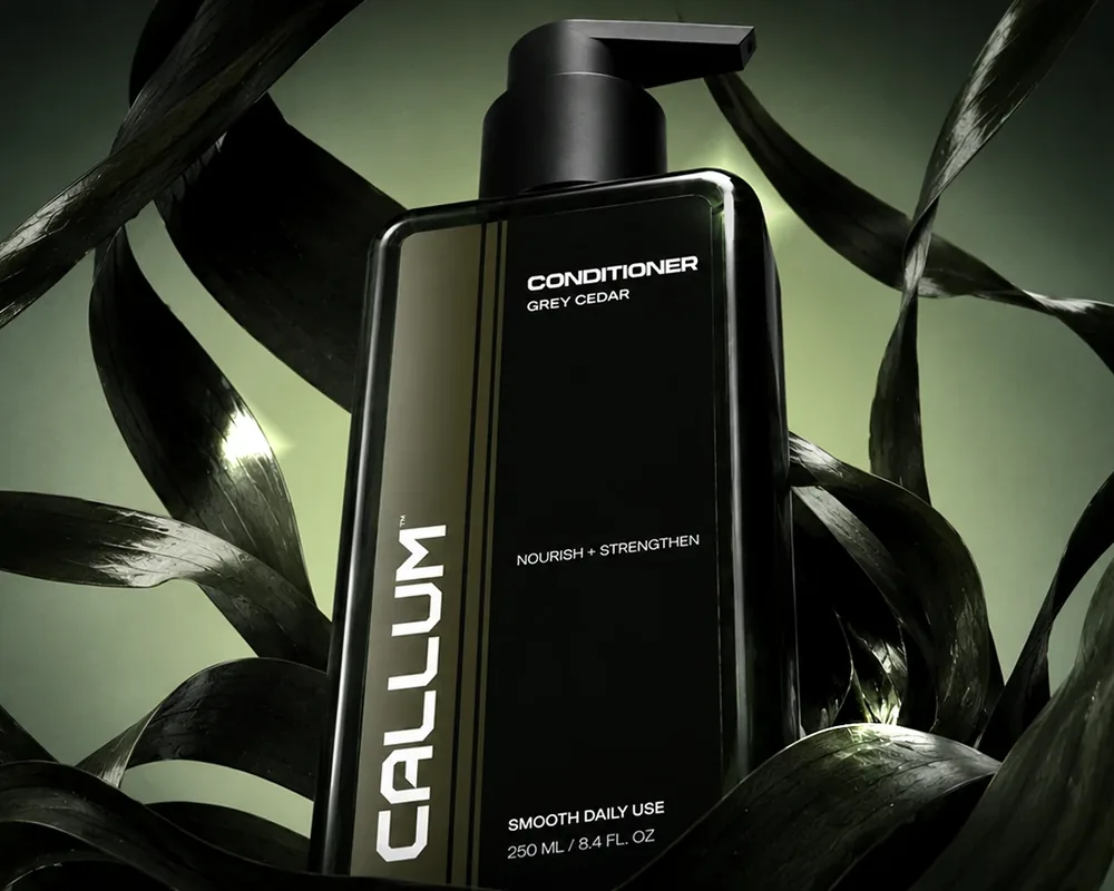 Dark green CALLUM conditioner bottle among leaves